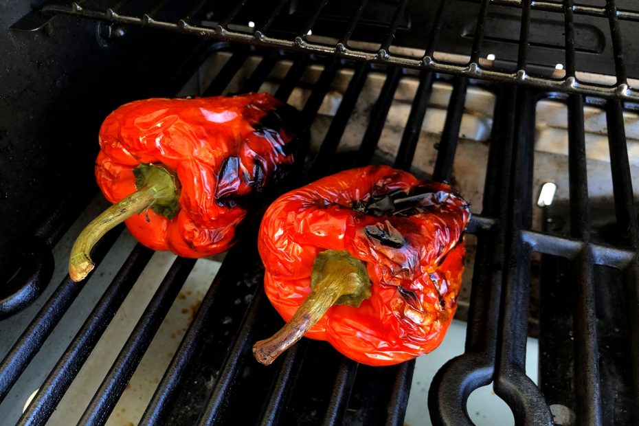 2 rote Paprikas auf dem Grillrost mit teils verbrannter Haut